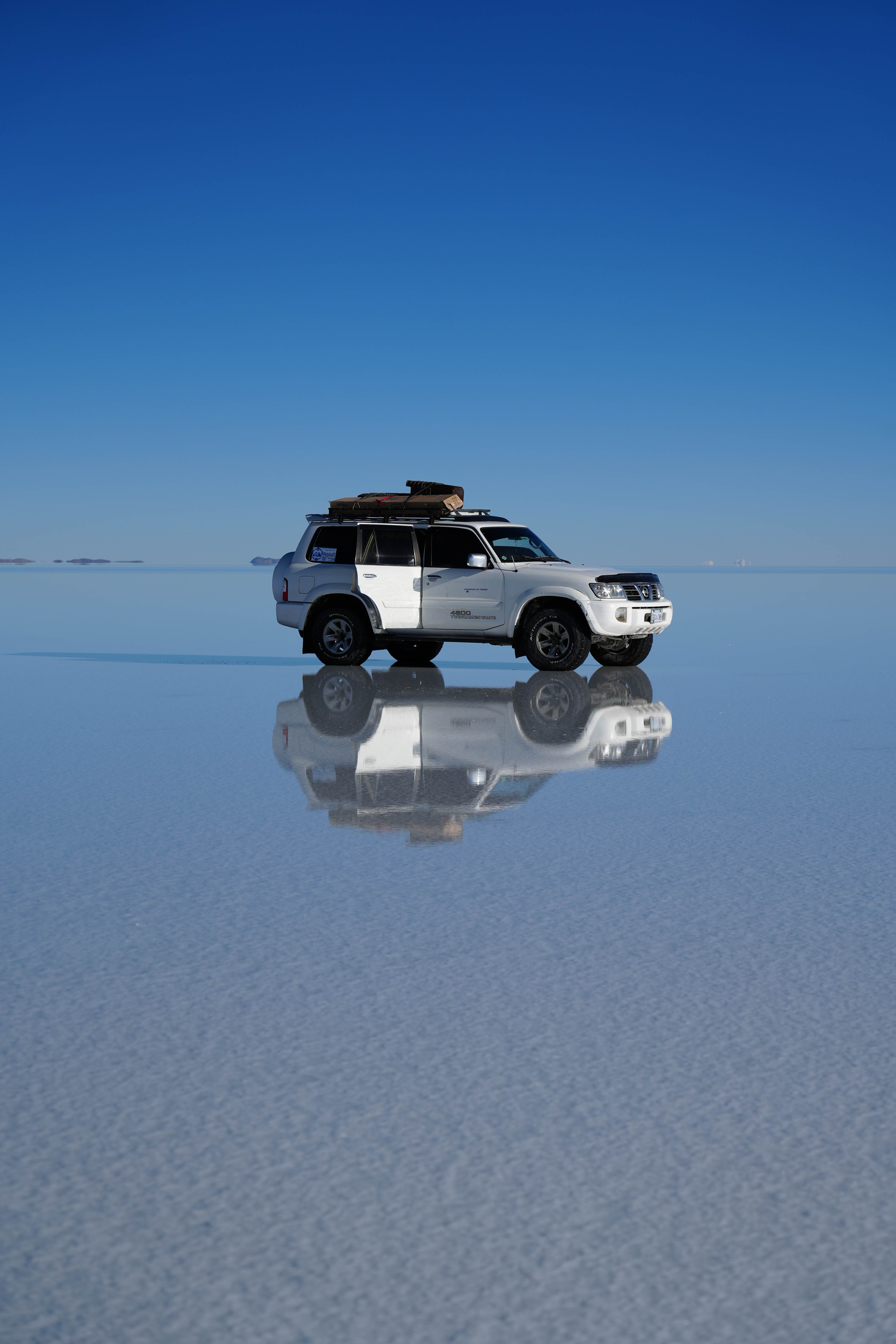 Vehículo todoterreno blanco reflejado sobre el espejo de agua del Salar de Uyuni.